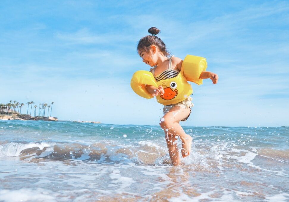 Young girl enjoying the beach with floaties and water splashes.