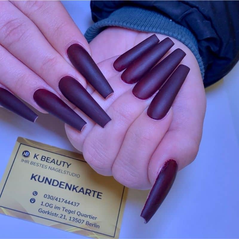 Dunkelrote, matte Gel-Nägel auf einer Hand, professionell gestaltet.