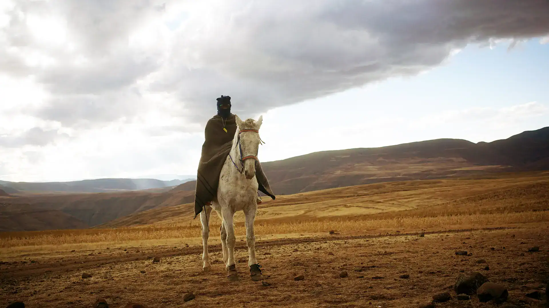 Ancient warrior riding a horse across a vast, open landscape with rolling hills and dramatic clouds.