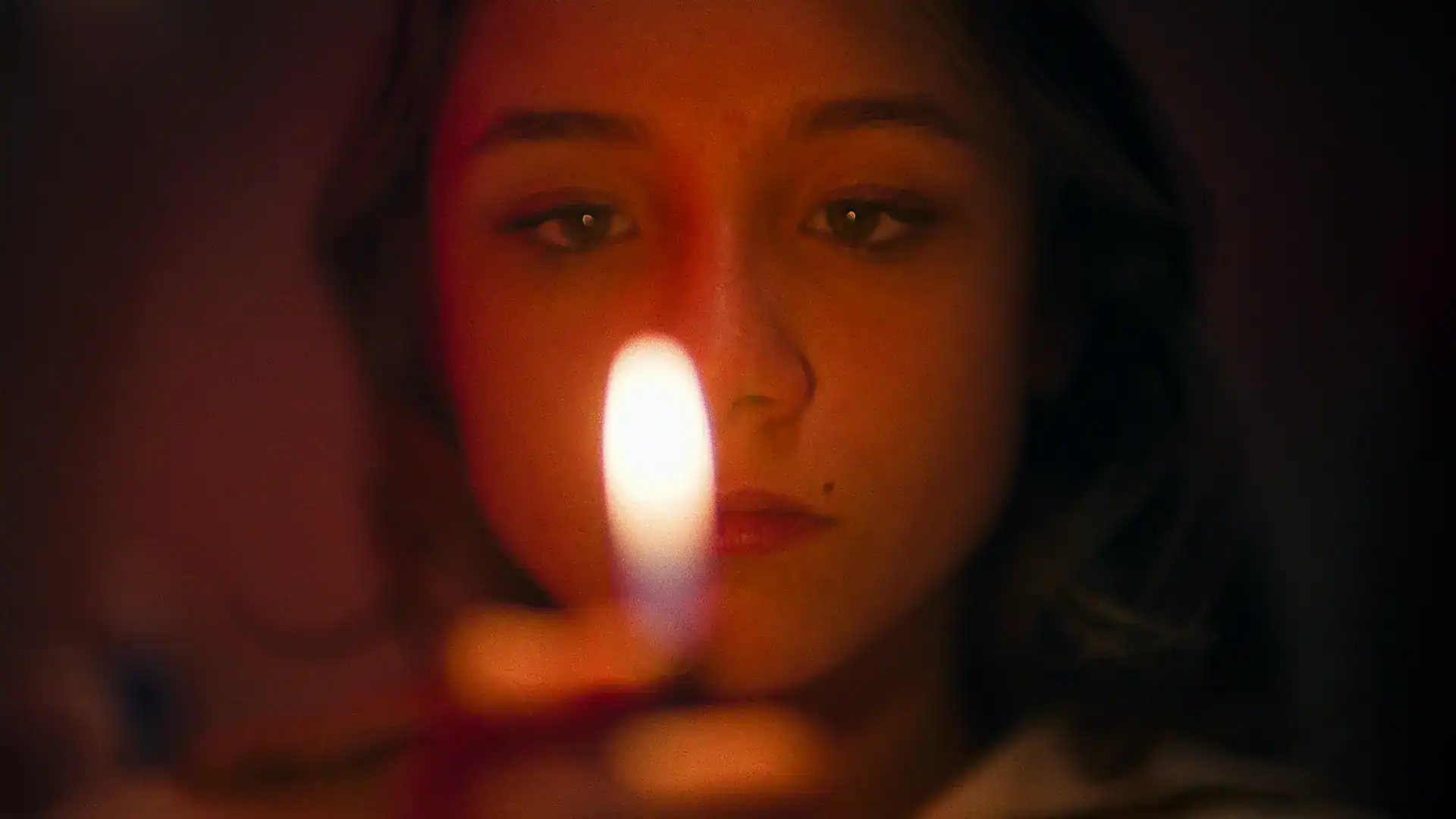 Young woman holding a candle in a dark setting.