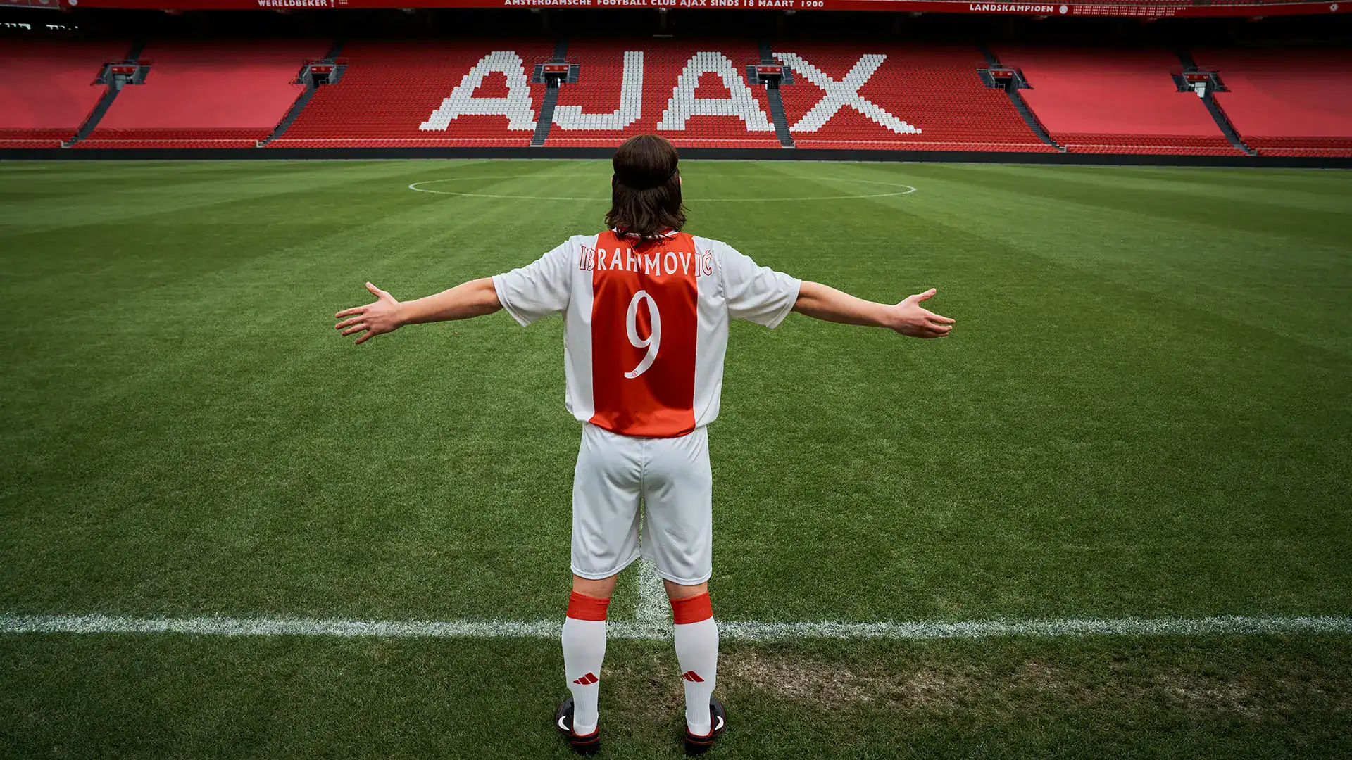 Ajax football player celebrating on the pitch with arms outstretched.