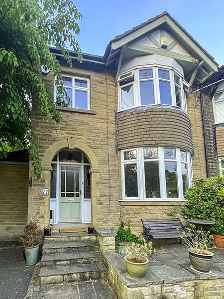 Exterior of 72 Morris Lane, a stone semi-detached house with a curved bay window, and stone paving with four steps up to an arched front door.