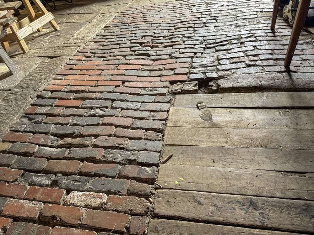 The interior of the barn at Hollybush. It shows the different kinds of flooring, worn brick work, floorboards, and stone paving slabs.
