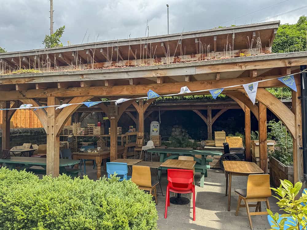 Outside at Hollybush showing a large wooden shelter with tables and chairs beneath it.