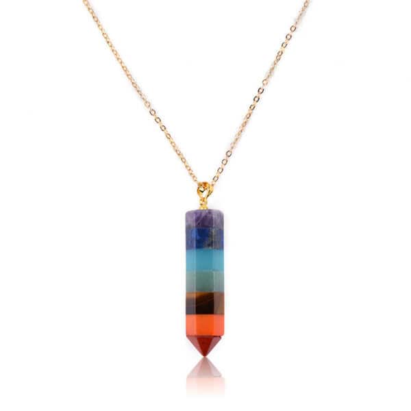 The Seven Chakra Point Pendant is a gold chain necklace featuring a vertical, hexagonal pendant with stacked purple, blue, green, yellow, orange, and red crystals in a pointed design.