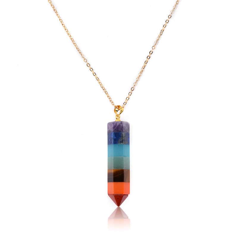The Seven Chakra Point Pendant is a gold chain necklace featuring a vertical, hexagonal pendant with stacked purple, blue, green, yellow, orange, and red crystals in a pointed design.