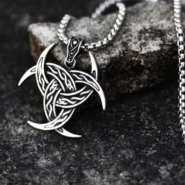 The Triple Horn of Odin Pendant Amulet Necklace features an intricate Celtic knot design with crescent points, inspired by Norse mythology, shown resting on a textured dark stone surface.