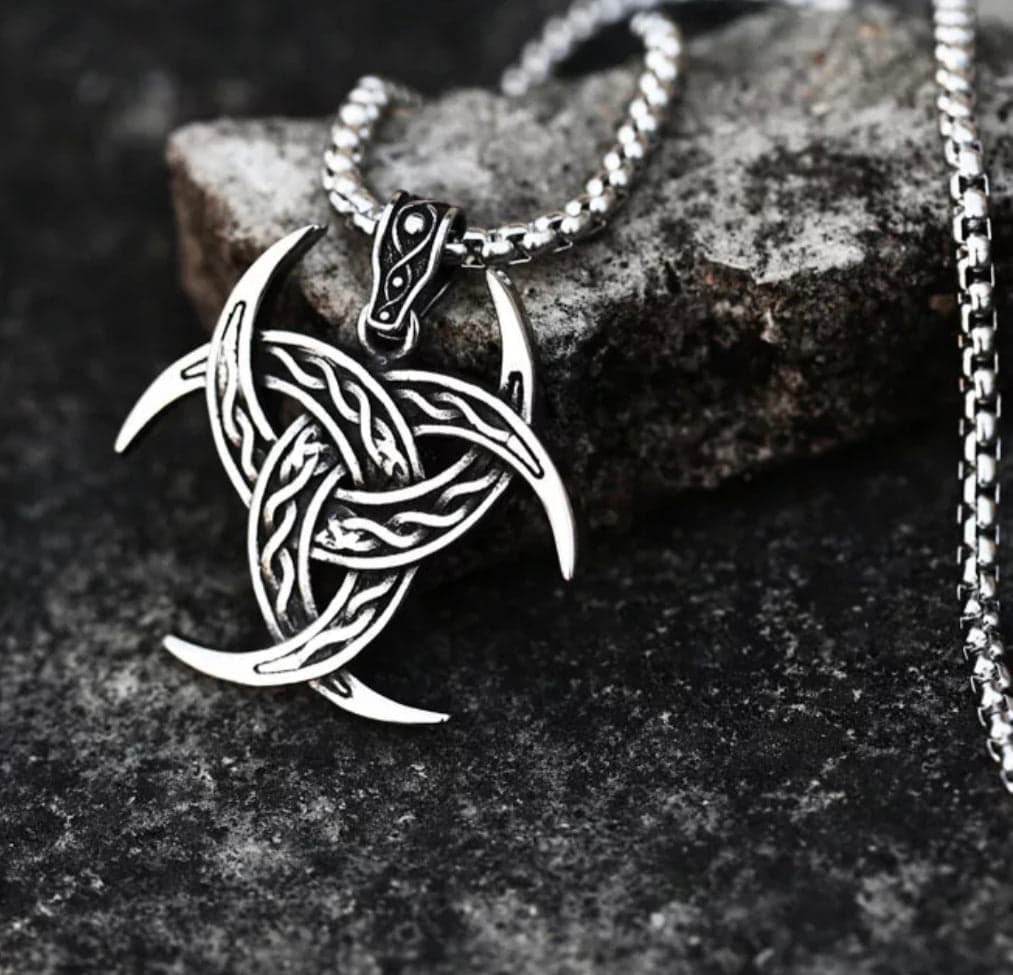 The Triple Horn of Odin Pendant Amulet Necklace features an intricate Celtic knot design with crescent points, inspired by Norse mythology, shown resting on a textured dark stone surface.