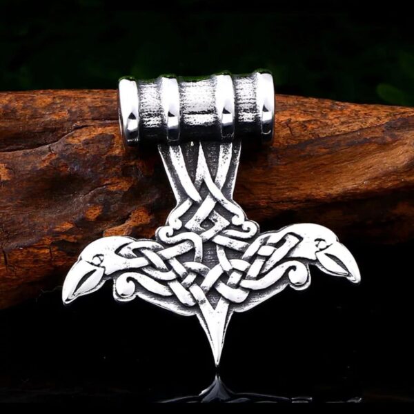The Odins Ravens Pendant Amulet Necklace features a silver Thor’s hammer with Norse knotwork, stylized animal heads, and subtle Odin’s ravens, displayed on wood against a dark background.