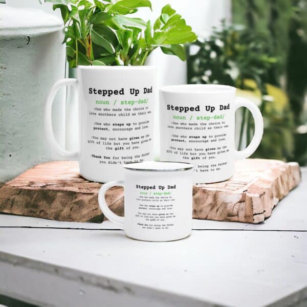 Three Stepped Up Dad Mugs featuring a witty definition in black and green text are arranged on a white table next to green plants and wooden decor.