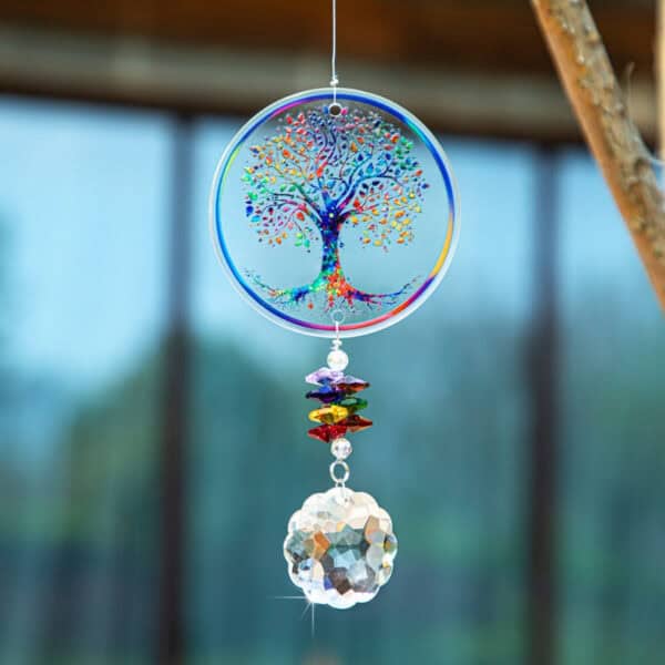 The Chakra Tree of Life Suncatcher, decorated with vibrant crystal beads and a faceted crystal ball, hangs beautifully and sparkles in sunlight against a softly blurred outdoor backdrop.