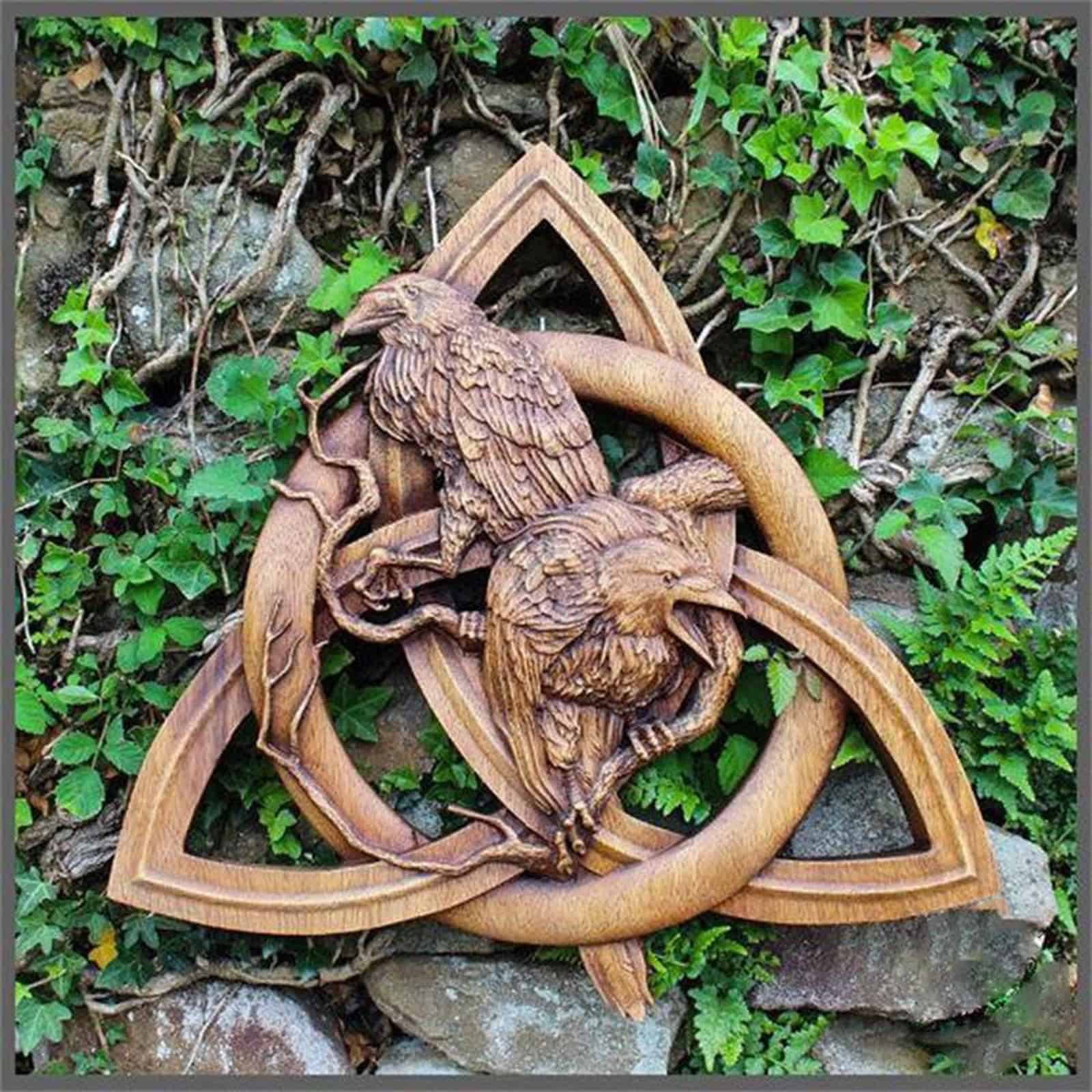 The Odin Ravens Wall Carving features two wooden ravens on intertwined branches within a Celtic triquetra knot, perfect for hanging on any wall adorned with ivy and ferns.