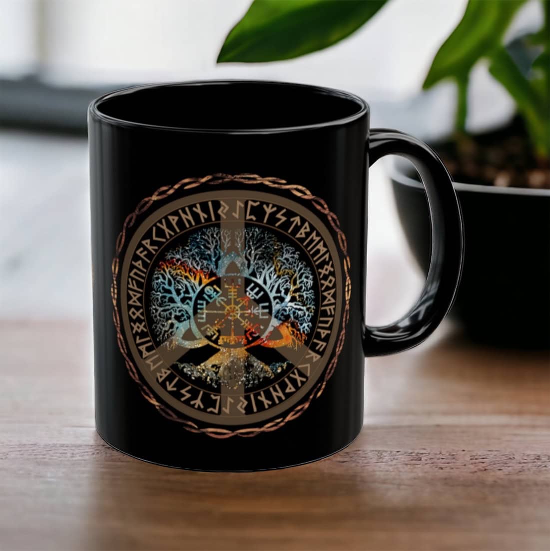 A Vegvisir Worldtree Black Ceramic Mug with a vibrant Norse design, showcasing Yggdrasil and runes, rests on a wooden table next to a small black plant pot.