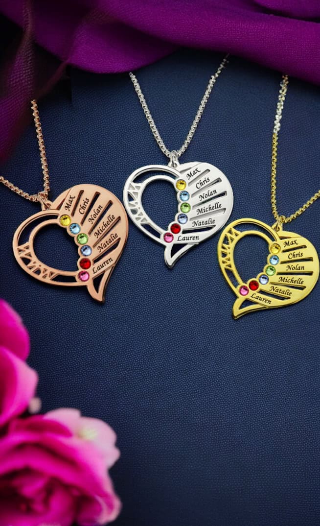 The Multi Name with Birthstones Heart Necklace features gold, silver, and rose gold heart pendants engraved with Max, Chris, Nolan, Michelle, Natalie, and Lauren beside colorful gemstones on dark fabric with a purple drape and pink flowers.