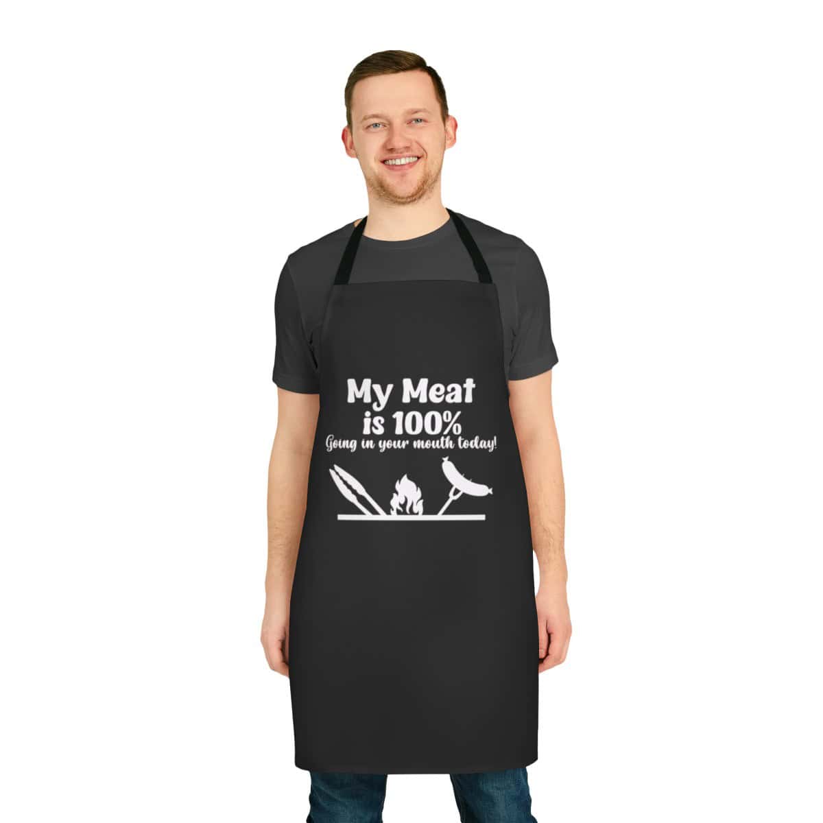 A smiling man wears a black My Meat is 100% Going in Your Mouth BBQ Apron featuring the phrase My Meat is 100% Going in your mouth today! with white graphics of grilling utensils, a flame, and a sausage.