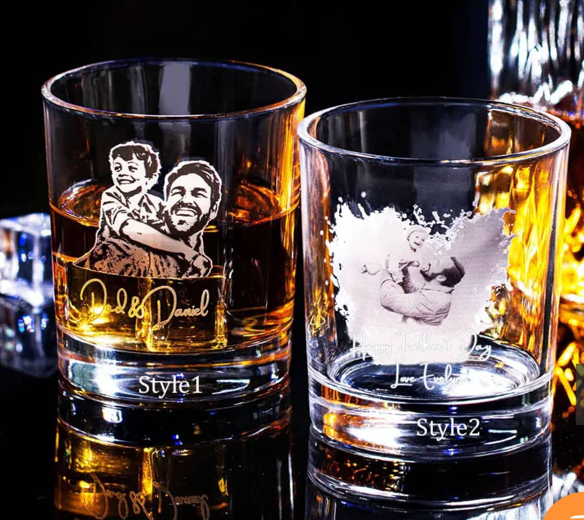 Two Engraved Photo Whiskey Glasses with drinks: the left glass features a custom image of a man carrying a child and the names Dad & Daniel; the right reads Happy Father’s Day, Love Luke with an etched man holding a child.