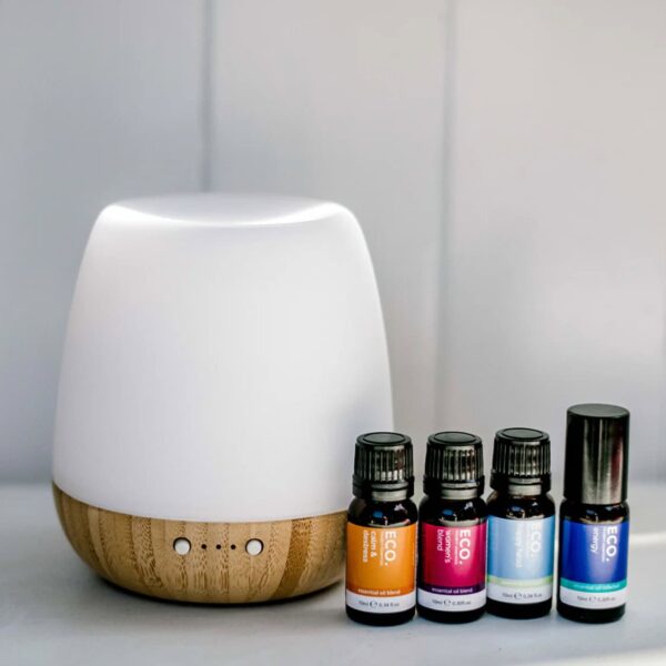The Revive & Thrive Aromatherapy Bundle features a white and bamboo essential oil diffuser beside four essential oils with colorful labels, all arranged on a white surface against a light gray background—ideal for enhancing your aromatherapy experience.