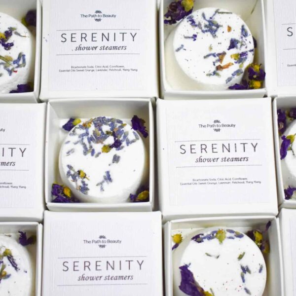 A top-down view of boxed Serenity Individual Shower Steamers, each adorned with dried flower petals. The boxes are arranged in a grid pattern and labeled “Serenity Individual Shower Steamers.”.