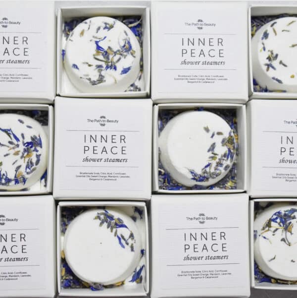 A grid of boxed Inner Peace Individual Shower Steamers—each round, white tablet topped with dried blue and yellow petals—displayed neatly in white packaging.
