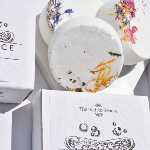 Three round white Single Bath Fizzers topped with dried flowers are displayed next to two white boxes labeled The Path to Beauty, each featuring a bubble illustration.