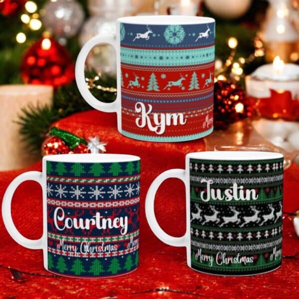 Three Ugly Sweater Christmas Mugs, personalized with “Kym,” “Courtney,” and “Justin,” are shown in front of a decorated Christmas tree. Two mugs feature a festive Merry Christmas message.