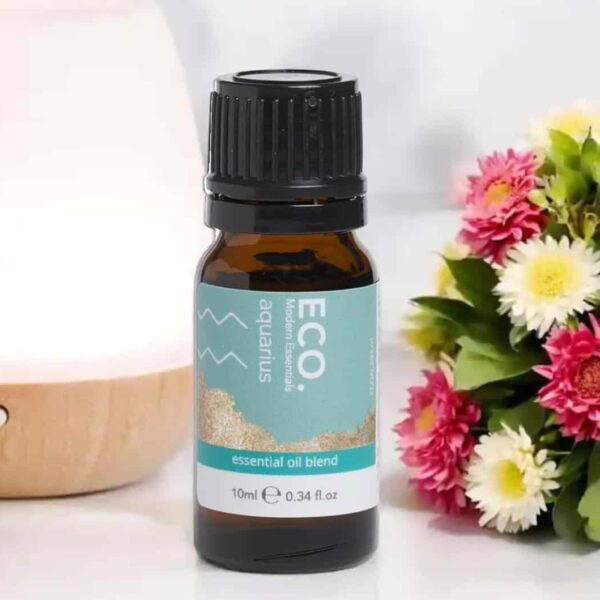 A 10ml (0.34 fl. oz) bottle of Aquarius Zodiac Essential Oil Blend rests on a white surface beside colorful flowers and a wooden diffuser.