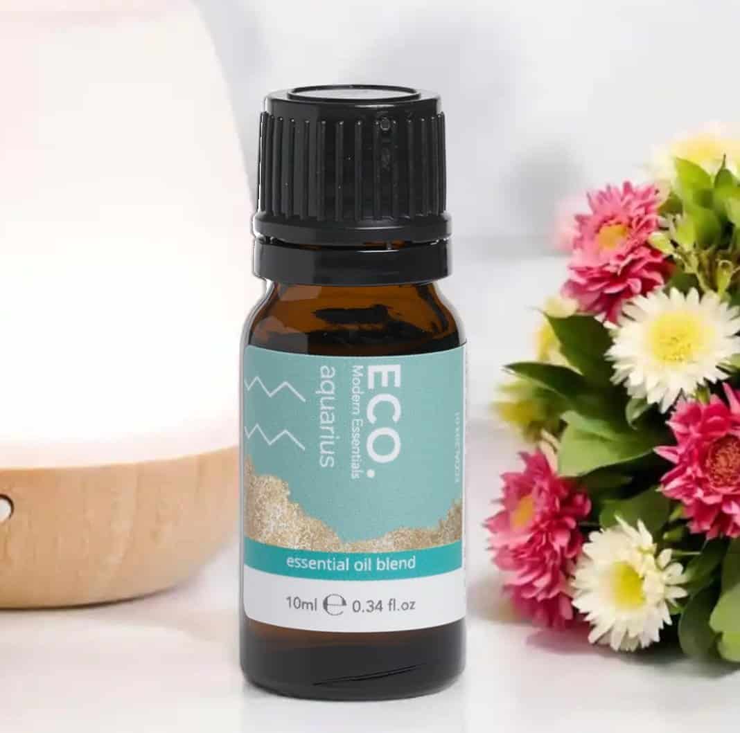 A 10ml (0.34 fl. oz) bottle of Aquarius Zodiac Essential Oil Blend rests on a white surface beside colorful flowers and a wooden diffuser.