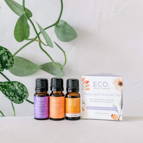 Three bottles from the Relax and Unwind Essential Oil Trio Pack are arranged on a white surface, surrounded by green vine leaves, inviting relaxation and calm.