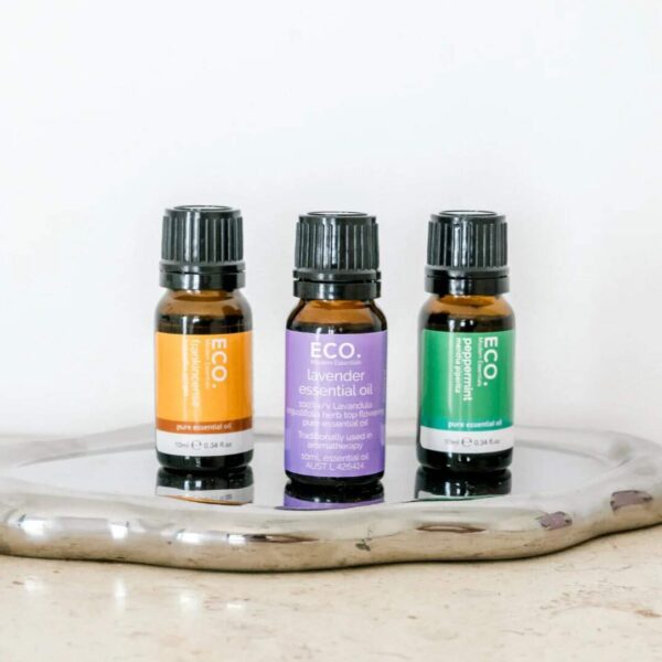 Three bottles from the Classic Essentials Trio Essential Oil Pack—orange, lavender, and peppermint—are displayed on a shiny silver tray against a white background.