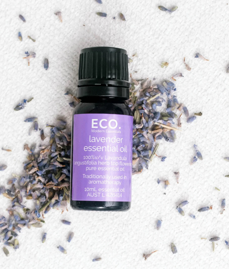 A bottle of Lavender Essential Oil rests on a white surface, surrounded by scattered dried lavender buds.
