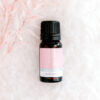 A 10ml bottle of ECO Little Pick Me Up Essential Oil Blend sits on a soft white textured surface, accented by delicate pink-tinted foliage on the left.