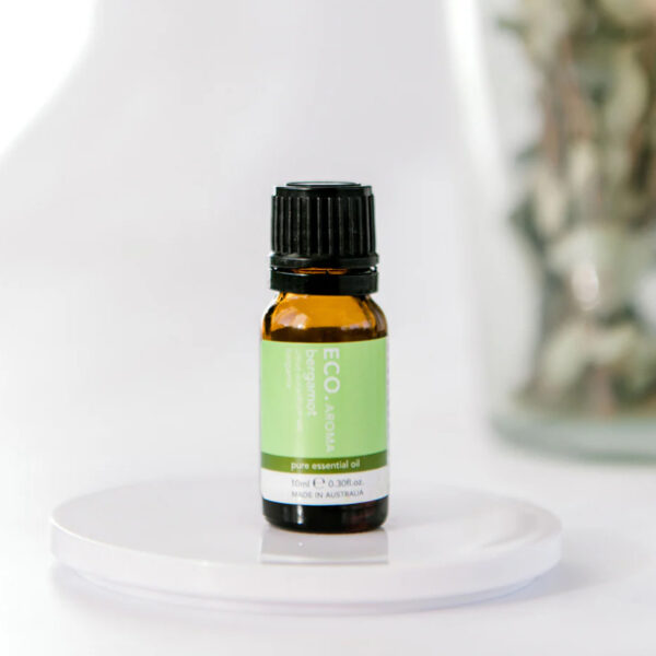 A small amber glass bottle of Bergamot Pure Essential Oil rests on a white surface with a blurred background.