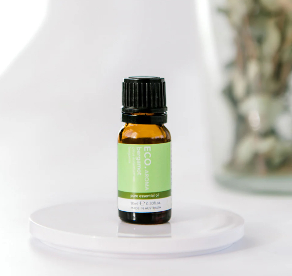 A small amber glass bottle of Bergamot Pure Essential Oil rests on a white surface with a blurred background.