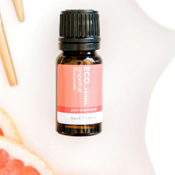 A small amber bottle of Grapefruit Pure Essential Oil rests on a white surface, surrounded by fresh grapefruit slices and two wooden sticks.