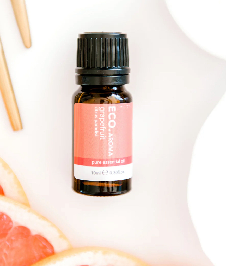A small amber bottle of Grapefruit Pure Essential Oil rests on a white surface, surrounded by fresh grapefruit slices and two wooden sticks.