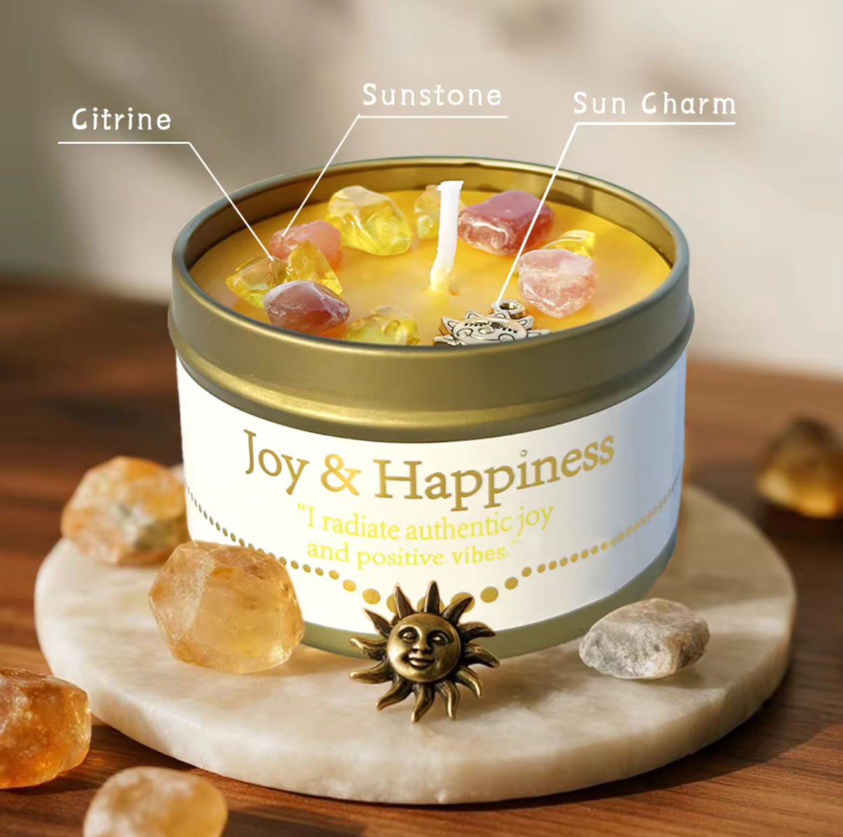 A yellow candle labeled Joy & Happiness sits on a round stone base, topped with citrine, sunstone, and a sun charm. Additional citrine stones and a sun charm are placed around the candle.