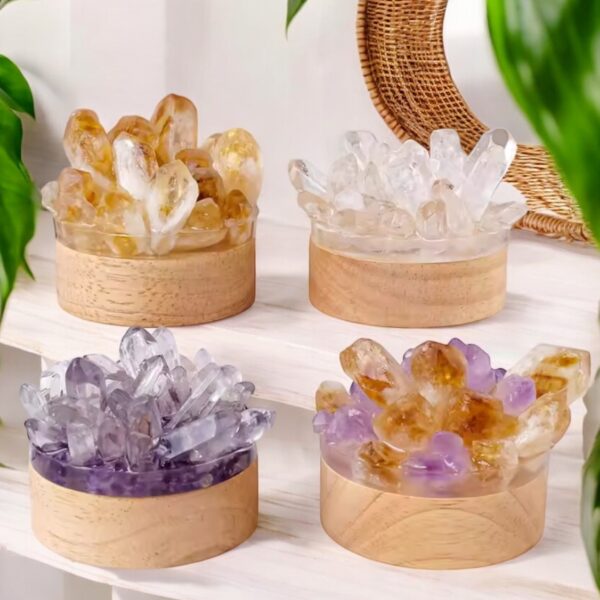 Four round wooden containers hold Natural Stone Point Mood Lamps in yellow, clear, purple, and amber hues. Theyre displayed on white shelves with green plants and a wicker-framed mirror in the background.
