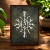 The Viking Stave For Dad Wooden Framed Print features a white, detailed Viking stave design on a dark textured background, framed in wood and displayed on a wooden surface with green plants beside it.