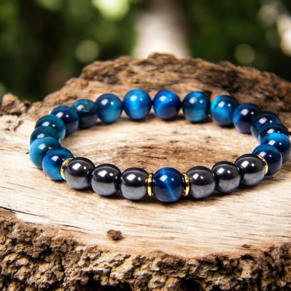 The Sapphire Tiger Eye Bracelet, featuring glossy blue and dark gray beads with gold spacers, is displayed on a textured tree stump against a blurred green background.