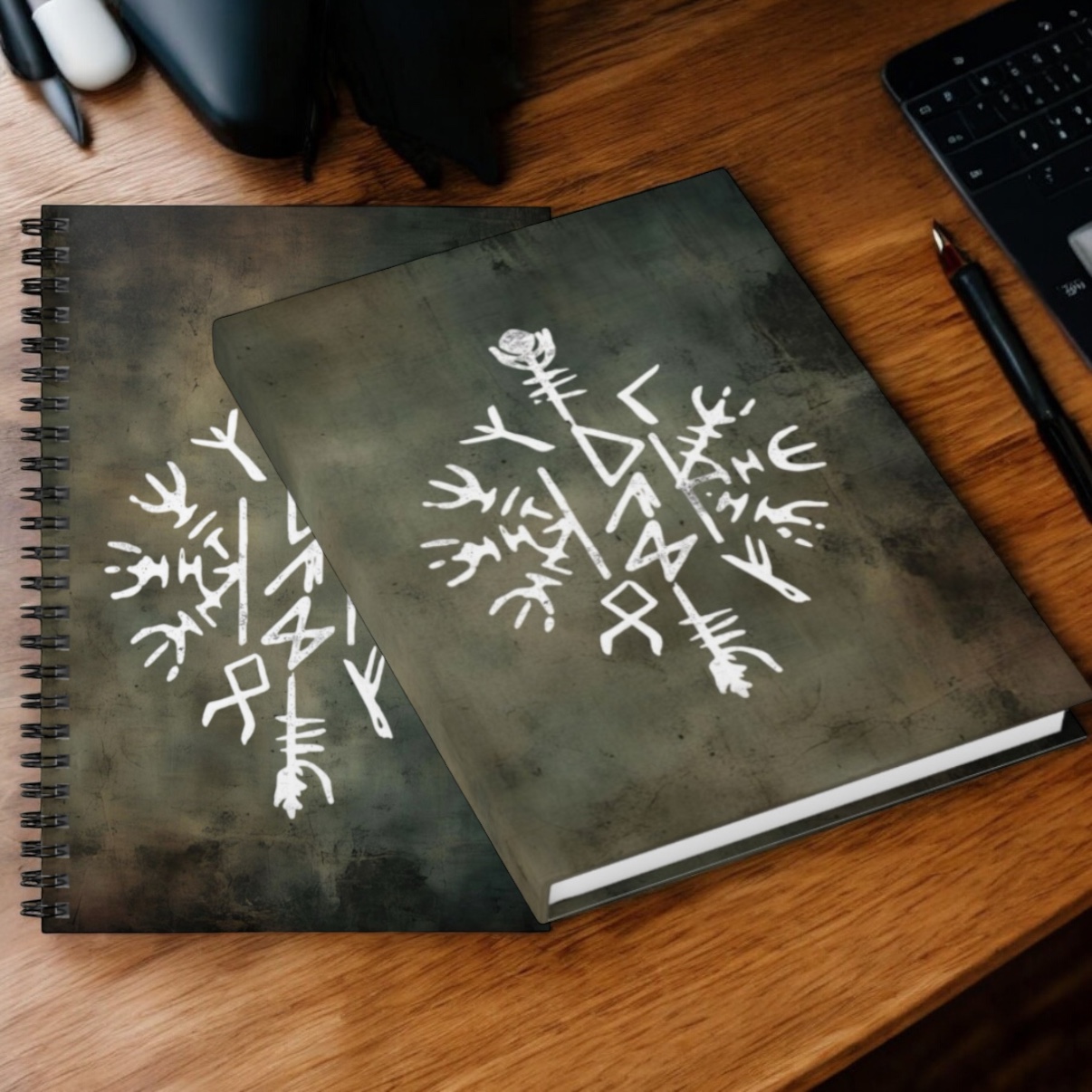 The Dad Viking Stave Journal & Spiral Notebook – Norse Rune Inspired features hardcover spiral notebooks with bold Norse designs, shown on a wooden desk beside a pen, tablet, and black pouch for a rugged Viking journal vibe.