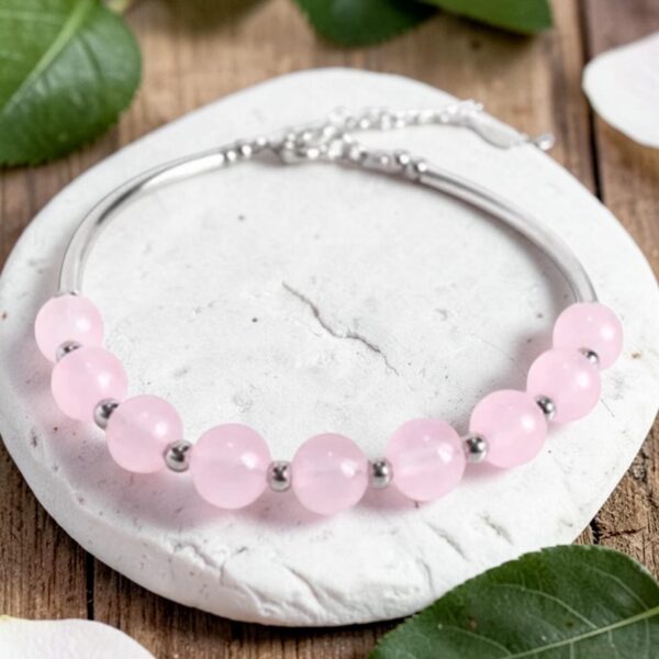 Natural Rose Quartz beads on a sterling silver bangle bracelet. The bracelet is displayed laying on a white stone