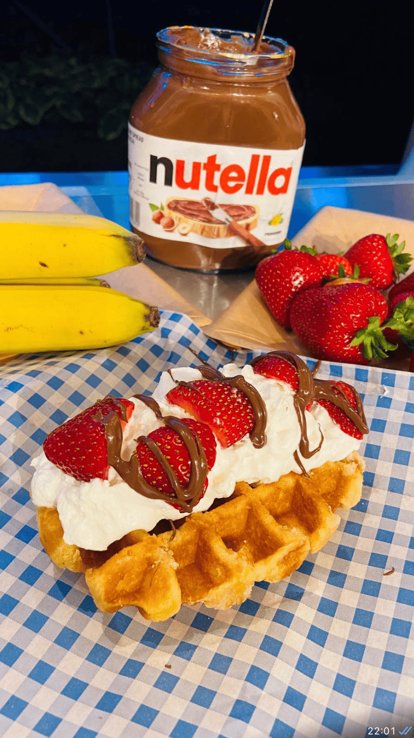 Nutella-stuffed waffle with strawberries and whipped cream, served with fresh fruit and bananas.