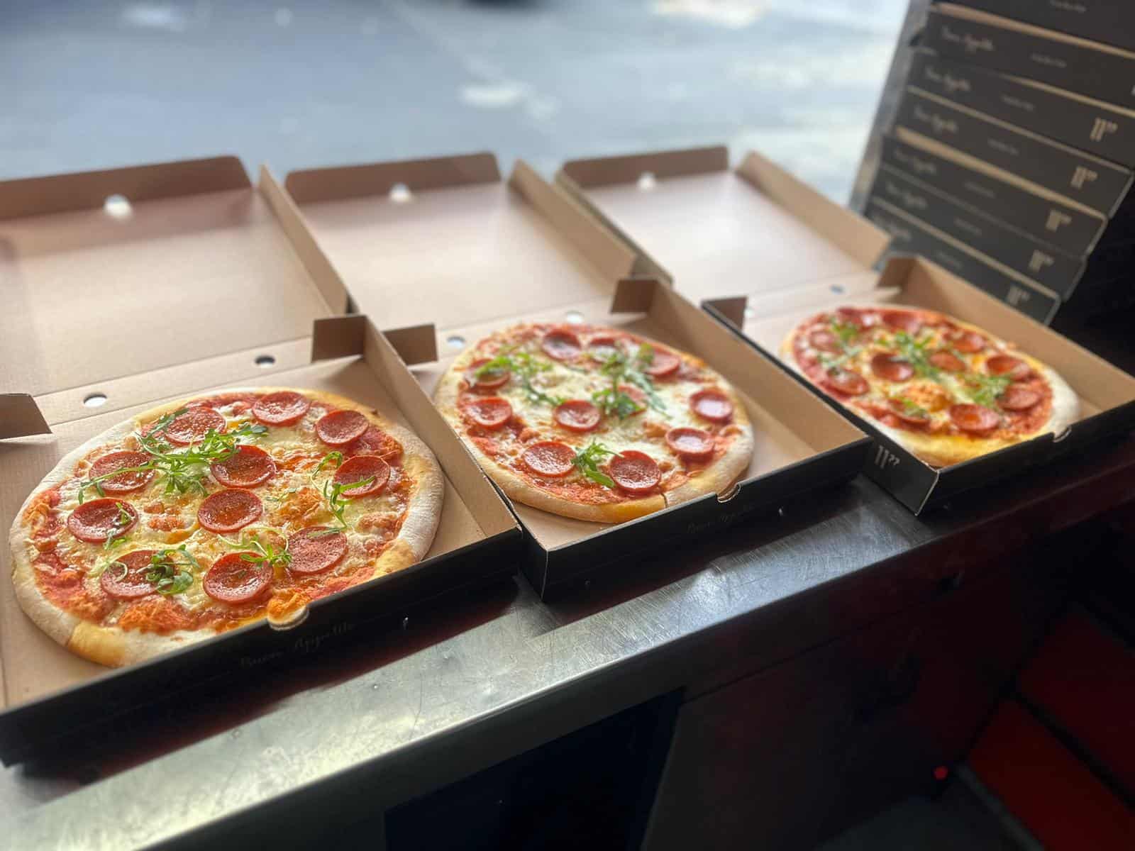 Three freshly cooked pepperoni pizzas in boxes on a KK Catering pizza van counter at a corporate event.