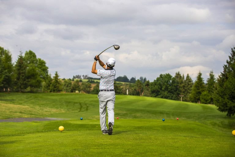 Golfspiller på green med natur i baggrunden.