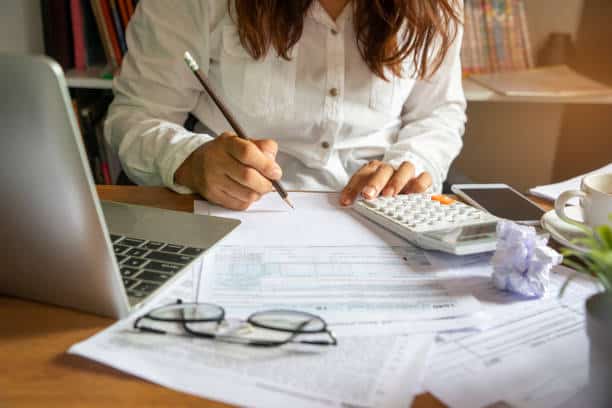 woman signing document with her laptop and calculator