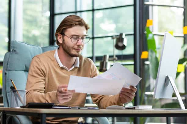 Serious and purposeful accountant financier on paper work in the office, young man goes through documents in his hands. 