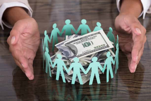 Advocacy Groups and Supporters Hand Protecting Paper Cut Out Human Figures Around Stack Of Hundred Dollar Bills