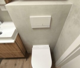 Podwieszana miska WC na stelażu podtynkowym z czarnym przyciskiem spłukującym i półką wykończoną drewnem.
