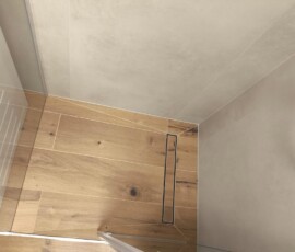 Strefa prysznicowa walk-in z czarną deszczownicą na tle ciepłych płytek imitujących naturalne drewno.