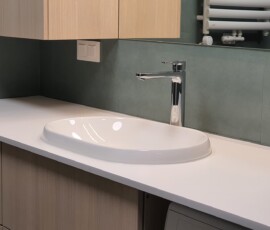 Okrągłe lustro z podświetleniem LED i biała umywalka na drewnianym blacie łazienkowym.